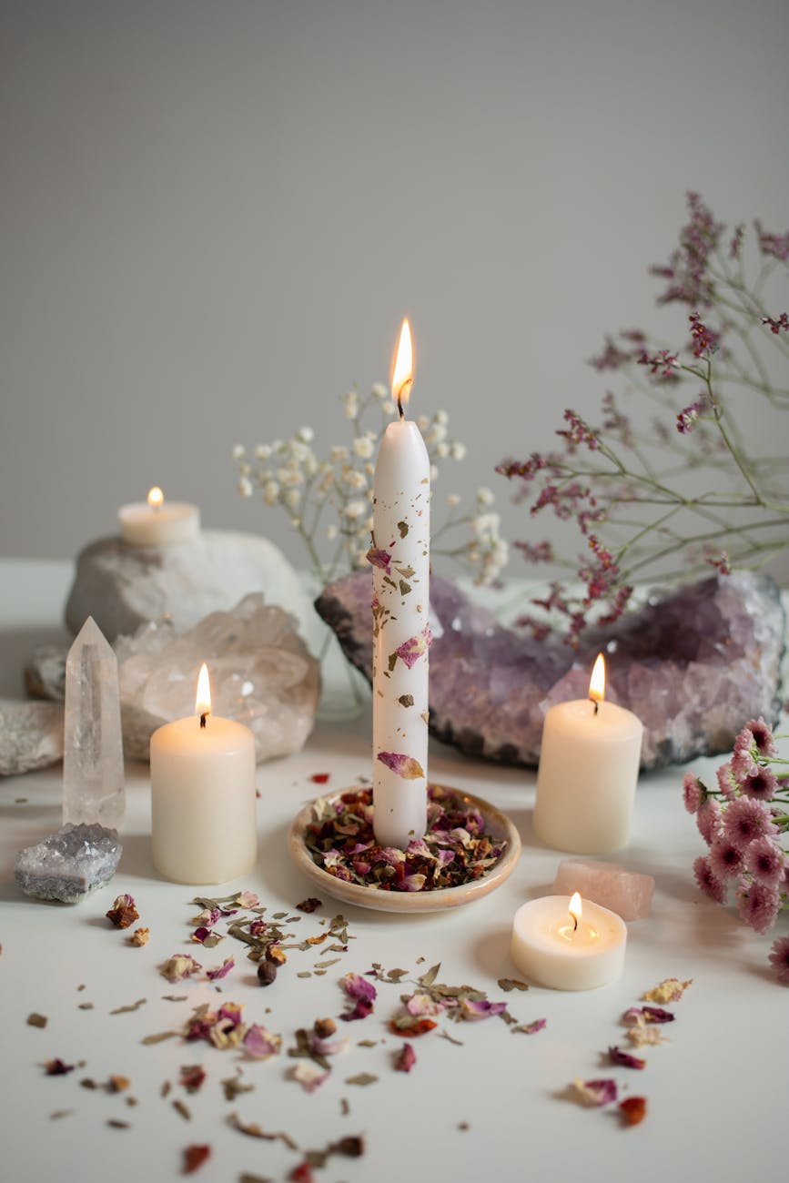 burning candles flowers and crystals lying on a white table