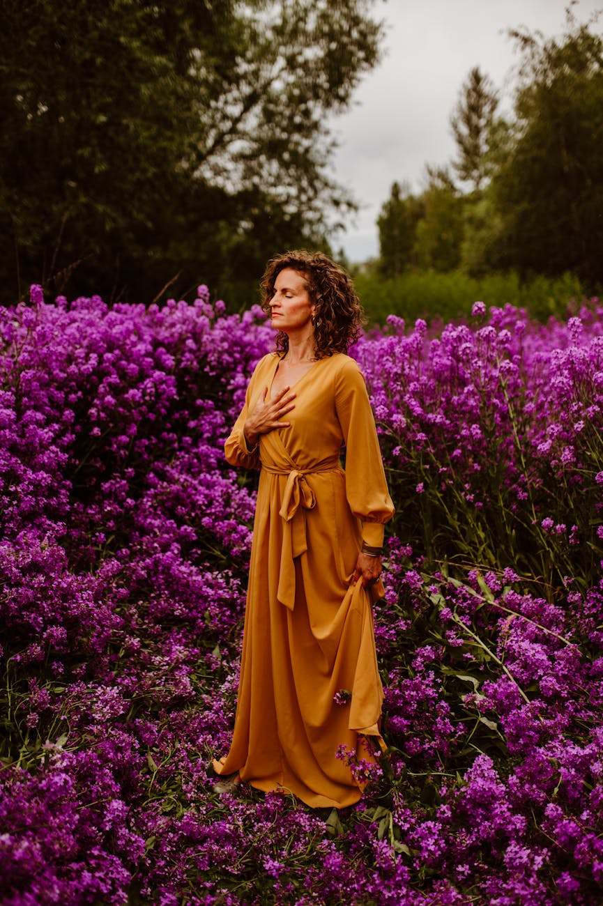 woman in orange dress amidst purple flowers. honoring midlife
