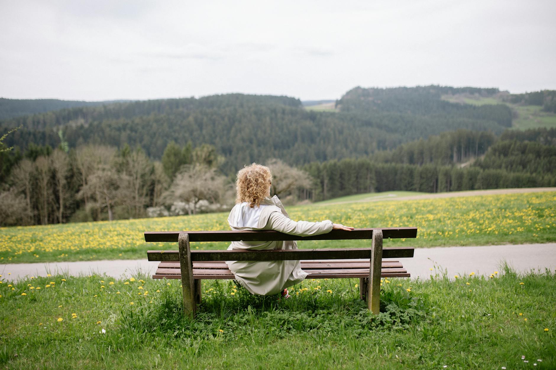 back view of a woman sitting alone on a wooden bench