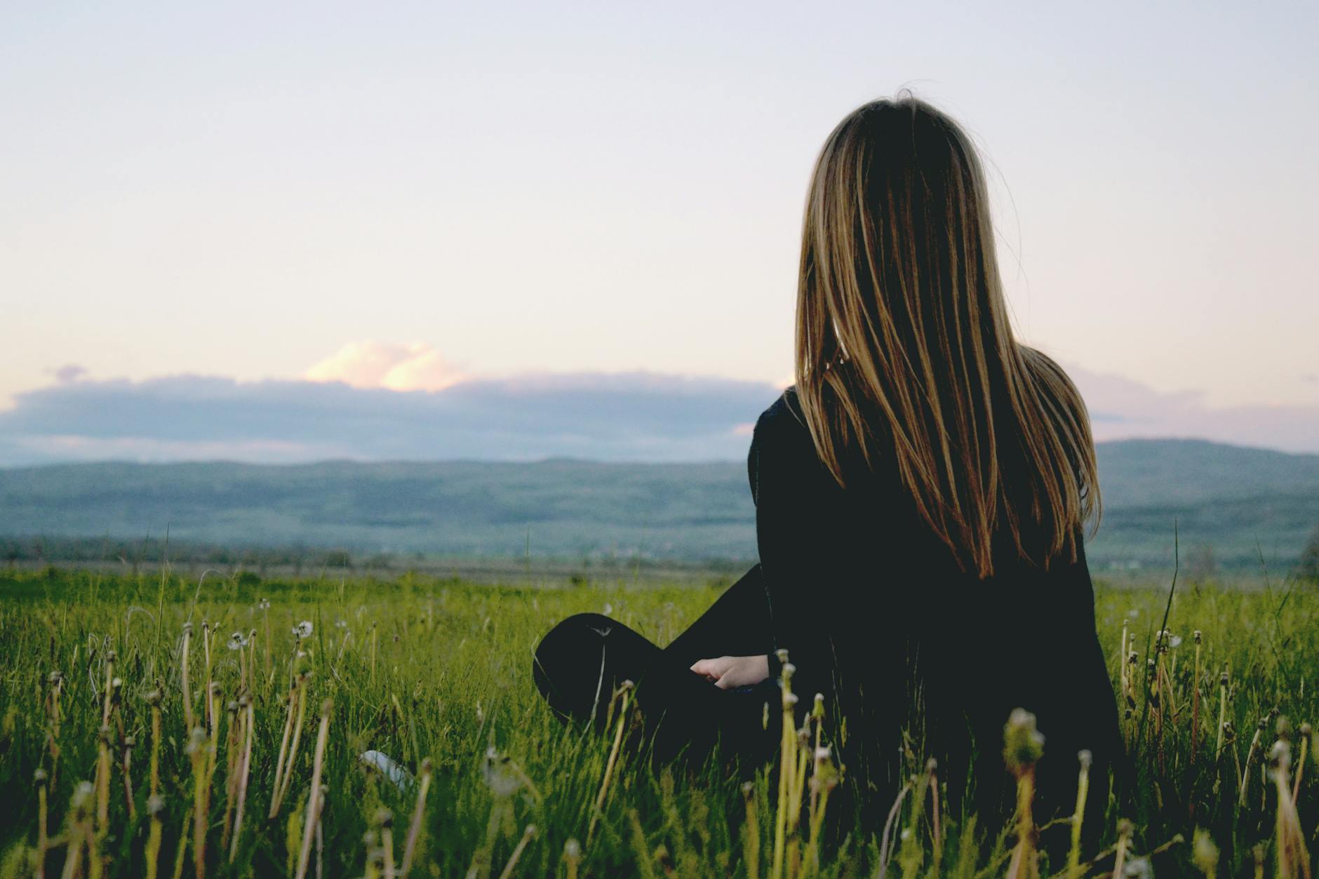 woman wearing black long sleeved shirt sitting on green grass field. midlife
