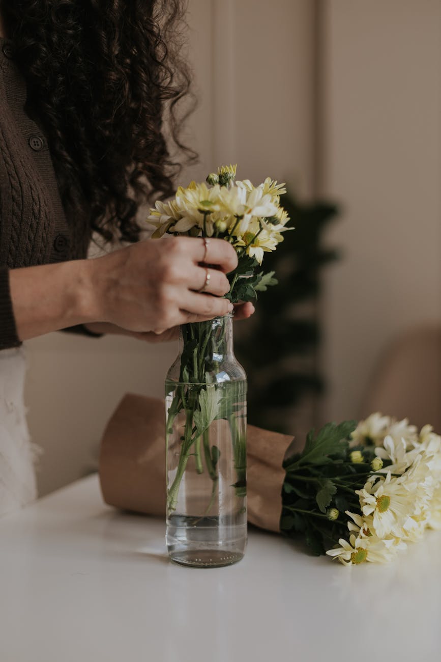 woman arranging yellow flowers in glass vase